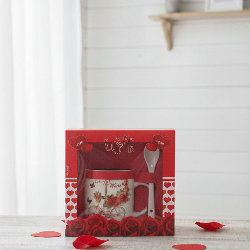 Red gift box with a mug and spoon set on a white surface with red heart decorations.