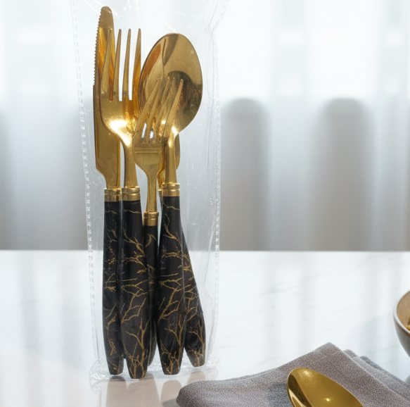 Set of gold and black patterned cutlery in a clear plastic bag on a white surface.